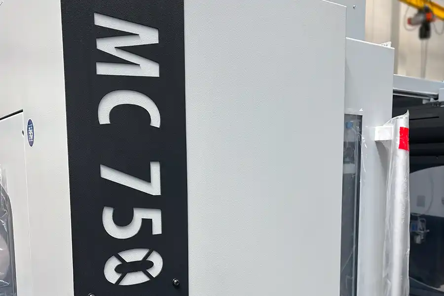 Detail centrum frezarskiego CNC MC 750 z oznaczeniem modelu i solidną obudową maszyny Detail centrum frezarskiego CNC MC 750 z oznaczeniem modelu i solidną obudową maszyny